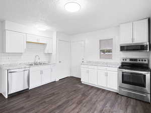 Kitchen featuring stainless steel appliances, backsplash, white cabinetry, dark LVP flooring, and a textured ceiling