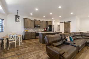 Kitchen featuring open floor plan, a barn door, backsplash, stainless steel appliances, and an island with sink