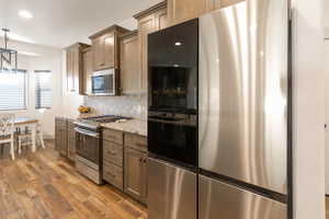 Kitchen featuring stainless steel appliances, light wood-style floors, hanging light fixtures, backsplash, and light stone counters