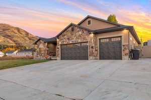 View of front of property with stone siding, driveway, a garage, and stucco siding
