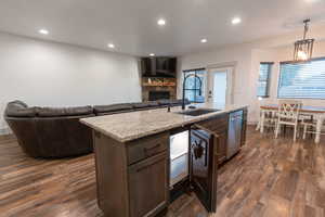 Kitchen with a stone fireplace, recessed lighting, open floor plan, light stone countertops, and dark brown cabinetry