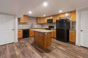Kitchen with black appliances, decorative backsplash, light stone countertops, brown cabinets, and recessed lighting