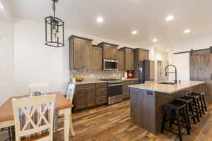 Kitchen with a barn door, backsplash, stainless steel appliances, a kitchen bar, and dark wood-style floors