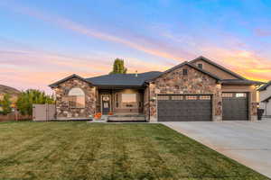 View of front facade featuring stone siding, a garage, a yard, concrete driveway, and covered porch