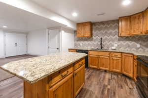 Kitchen featuring tasteful backsplash, a center island, light stone counters, brown cabinets, and recessed lighting