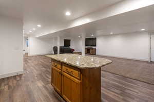 Kitchen featuring brown cabinetry, open floor plan, a center island, light stone counters, and recessed lighting