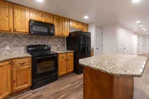 Kitchen with black appliances, dark wood-style flooring, brown cabinets, and recessed lighting
