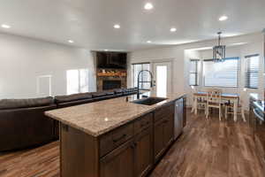 Kitchen with a stone fireplace, light stone countertops, recessed lighting, decorative light fixtures, and dark wood-style floors