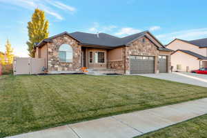 View of front of home with stone siding, a front lawn, a gate, and driveway