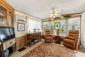 Sitting room with wooden walls, crown molding, a wainscoted wall, carpet floors, and a textured ceiling