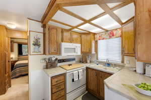 Kitchen featuring white appliances, tile countertops, brown cabinetry, light carpet, and coffered ceiling