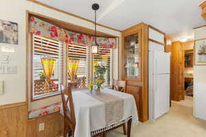 Dining space with wooden walls, a wainscoted wall, a textured ceiling, and light colored carpet