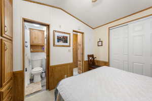 Bedroom featuring wood walls, lofted ceiling, a wainscoted wall, a closet, and ornamental molding