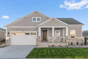 Craftsman house featuring a porch, stone siding, a garage, driveway, and a front yard