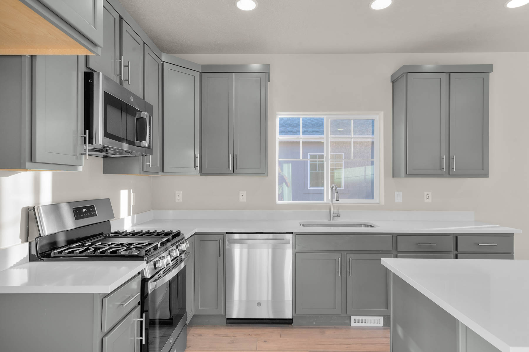 Kitchen featuring gray cabinetry, appliances with stainless steel finishes, recessed lighting, light wood-type flooring, and light stone counters