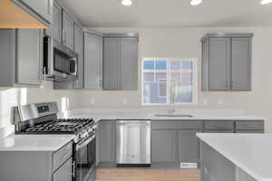 Kitchen featuring gray cabinetry, appliances with stainless steel finishes, recessed lighting, light wood-type flooring, and light stone counters
