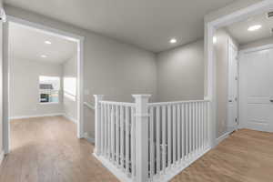 Corridor with an upstairs landing, light wood finished floors, and recessed lighting