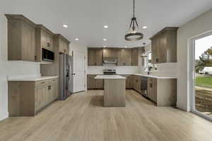 Kitchen with stainless steel appliances, hanging light fixtures, a kitchen island, light wood-style floors, and recessed lighting