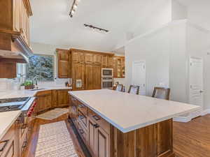 Kitchen featuring brown cabinets, a kitchen island, dark wood-style flooring, quartz counters, and appliances with stainless steel finishes