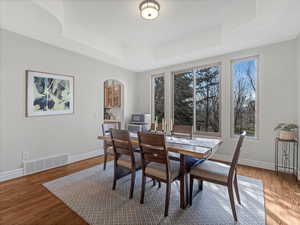 Dining room featuring a tray ceiling, hardwood floors, and arched walkways