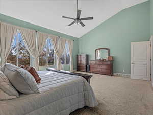 Carpeted bedroom featuring high vaulted ceiling and ceiling fan and lots of windows