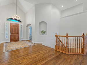 Entrance foyer featuring high vaulted ceiling, wood finished floors, a chandelier, and arched walkways