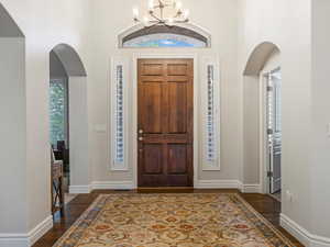 Entrance foyer with arched walkways, a towering ceiling, dark wood finished floors, and a chandelier