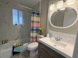 Full bathroom with vanity, shower / bathtub combination with curtain, backsplash, and light wood-style flooring