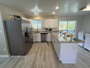 Kitchen with stainless steel appliances, a textured ceiling, a peninsula, light stone counters, and tasteful backsplash