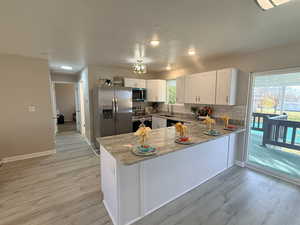 Kitchen with tasteful backsplash, a peninsula, light stone countertops, appliances with stainless steel finishes, and light wood-style floors