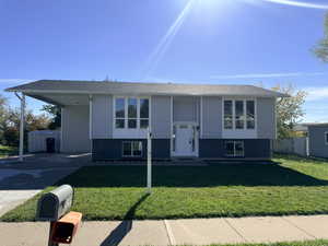 Split foyer home featuring a front yard, concrete driveway, a carport, and brick siding