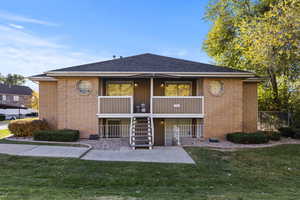 Front of property featuring stairs, brick siding, a lawn, and a balcony