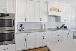 Kitchen featuring double oven, white cabinets, backsplash, and black electric stovetop