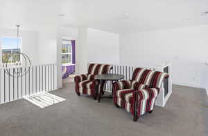 Sitting room with an upstairs landing, carpet floors, and a chandelier