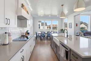 Kitchen with white cabinets, decorative light fixtures, custom exhaust hood, light stone counters, and recessed lighting