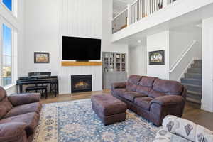 Living area featuring a towering ceiling, wood finished floors, stairs, and a large fireplace