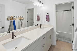 Full bath with double vanity, light tile patterned flooring, and shower / bath combo