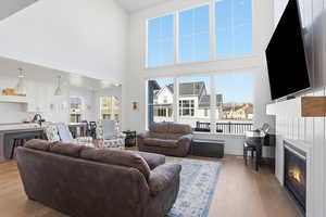 Living room with wood finished floors, healthy amount of natural light, a glass covered fireplace, and a towering ceiling