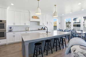 Kitchen with white cabinetry, stainless steel double oven, a kitchen breakfast bar, tasteful backsplash, and recessed lighting
