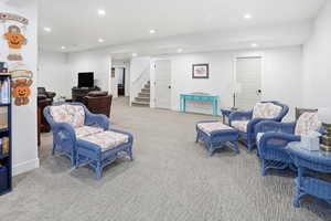 Carpeted living area with recessed lighting and stairway