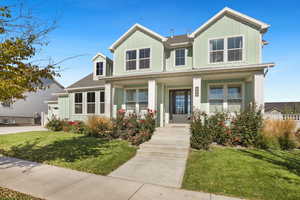 View of front of house with board and batten siding, covered porch, a front yard, and roof with shingles