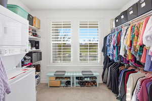 Walk in closet featuring light colored carpet and stacked washer / drying machine