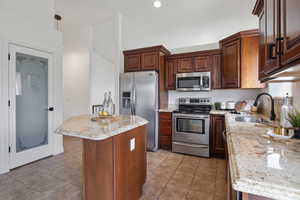 Kitchen featuring stainless steel appliances, a center island, light stone counters, decorative light fixtures, and light tile patterned floors