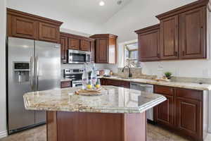 Kitchen with appliances with stainless steel finishes, light stone counters, a kitchen island, vaulted ceiling, and light tile patterned floors