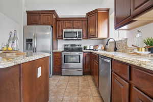 Kitchen featuring appliances with stainless steel finishes, light stone counters, and light tile patterned flooring