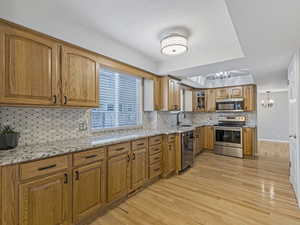 Kitchen featuring stainless steel appliances, light stone counters, glass insert cabinets, and light wood-style flooring