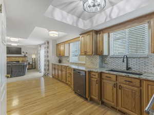 Kitchen with light stone counters, dishwasher, open floor plan, light wood-type flooring, and decorative backsplash