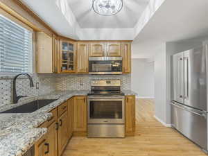 Kitchen featuring stainless steel appliances, light stone countertops, glass insert cabinets, and light wood-style flooring