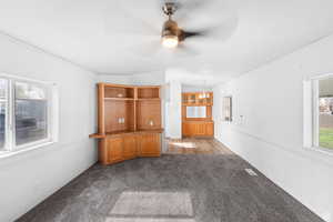 Unfurnished living room with dark colored carpet, vaulted ceiling, and ceiling fan