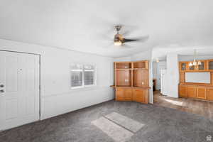 Unfurnished living room featuring ceiling fan, vaulted ceiling, dark carpet, and a chandelier